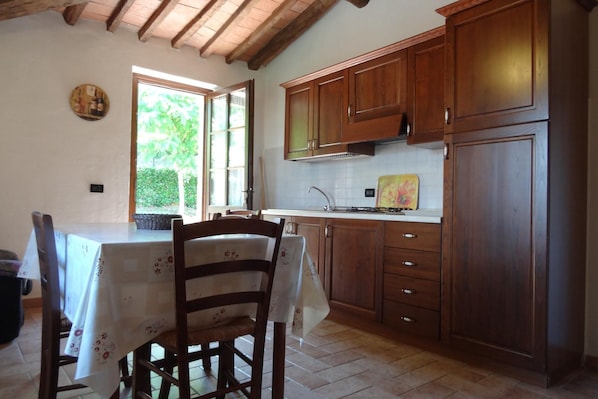 A kitchen with wooden cabinets, a white countertop, and a dining table with chairs. - Farmhouse Stay Giulia Volterra (Volterra)