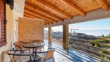 Ein Balkon mit Holzboden, einem runden Tisch mit Stühlen und Blick auf das Meer und Gebäude.
