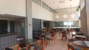 A spacious indoor dining area with multiple tables and chairs, high ceilings, and large windows.