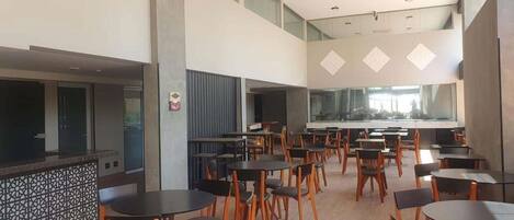 A spacious indoor dining area with multiple tables and chairs, high ceilings, and large windows.