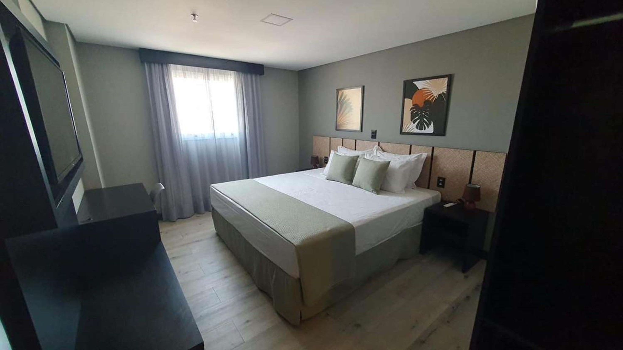 A hotel room with a large bed, a desk, a chair, a TV, and a window with curtains.