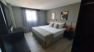 A hotel room with a large bed, a desk, a chair, a TV, and a window with curtains.