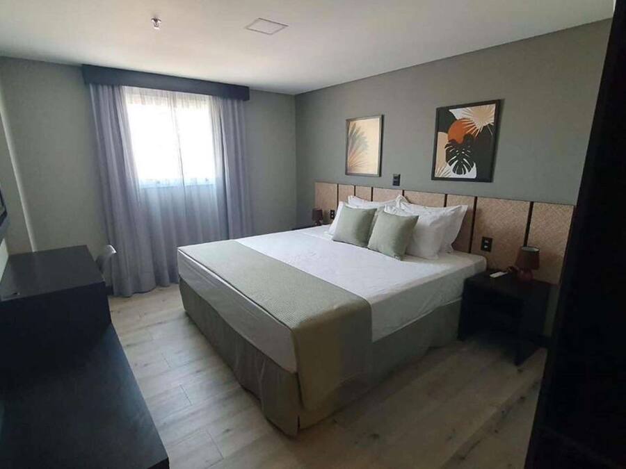 A hotel room with a large bed, a desk, a chair, a TV, and a window with curtains.