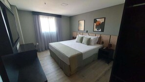 A hotel room with a large bed, a desk, a chair, a TV, and a window with curtains. - Tulip Inn Bauru (Bauru)