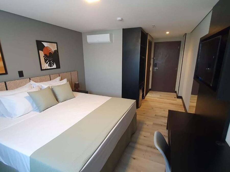 A hotel room with a large bed, a desk, a TV, and artwork on the walls.