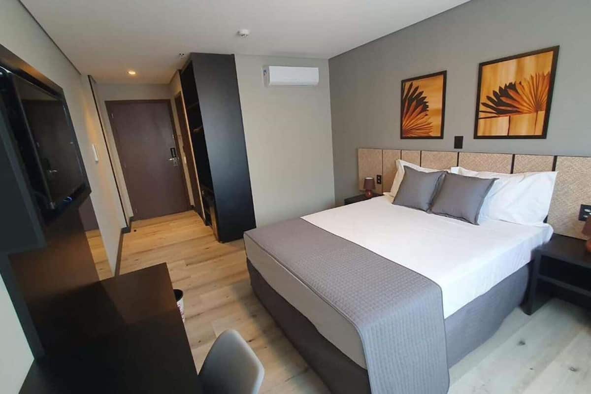 A hotel room with a bed, bedside tables, a desk, and artwork on the walls.