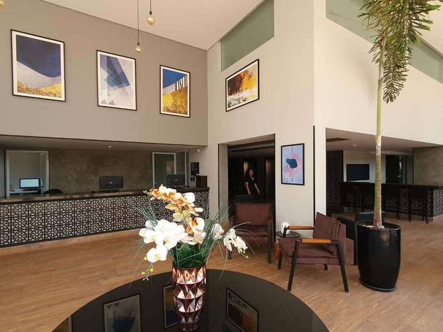 A hotel lobby with a reception desk, framed artwork on the walls, a large potted plant, and a seating area with chairs and a sofa.