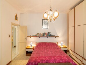 Ein Schlafzimmer mit Bett, Nachttischen, einer Hängelampe, einem Bücherregal und einer Tür.