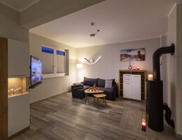 Ein modernes Wohnzimmer mit Flachbildfernseher, einer Couch, einem Couchtisch, einem Kamin und einer Küchenzeile mit Kühlschrank und Schränken.