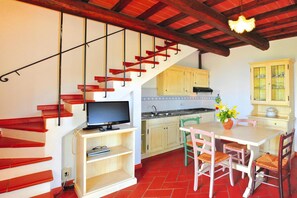 A kitchen with a wooden staircase, a dining table with chairs, and a television on a stand. - Borgo Collelungo, Apartments in Montaione (Montaione)