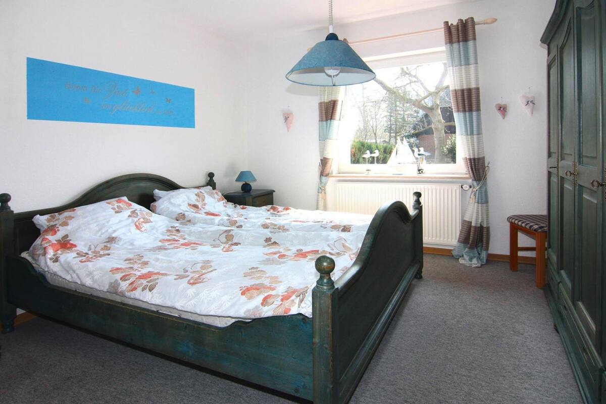 Un dormitorio con cama, mesita de noche, lámpara, ventana con cortinas y vistas al exterior.