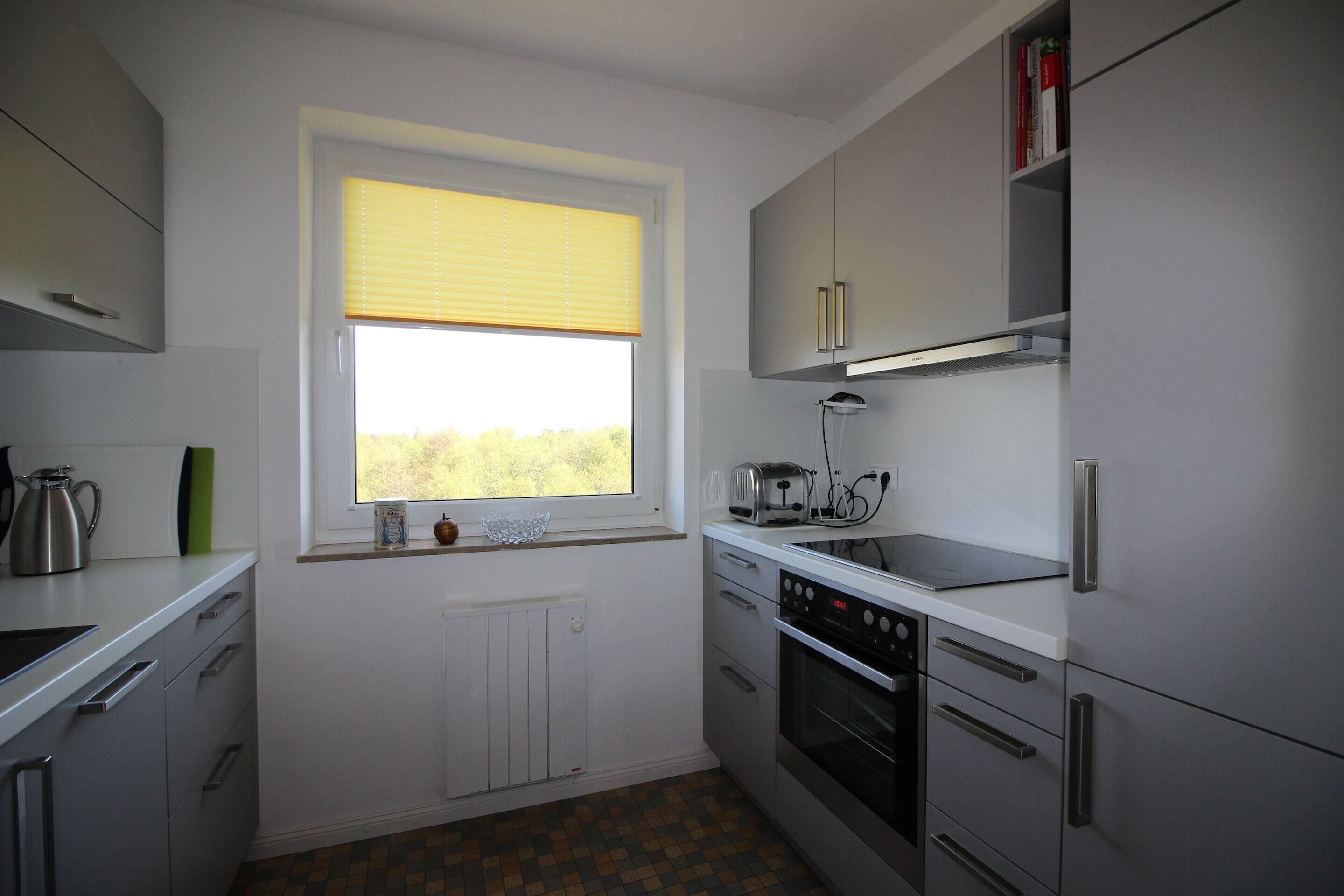 Eine moderne Küche mit weißen Schränken, einem Einbauofen und einem Fenster mit Jalousien.
