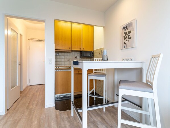 A compact kitchen with wooden cabinets, a microwave, and a small dining area with a white table and two chairs. - Apartment in St. Peter-ording (St. Peter-Ording)