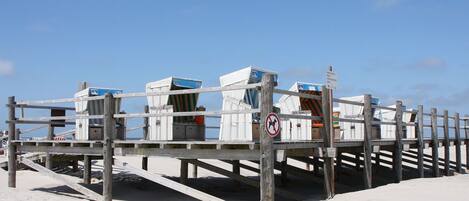 A beachside wooden structure with white wicker seating and a no swimming sign.