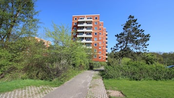 A multi-story building with a brick facade, surrounded by greenery and a paved path.