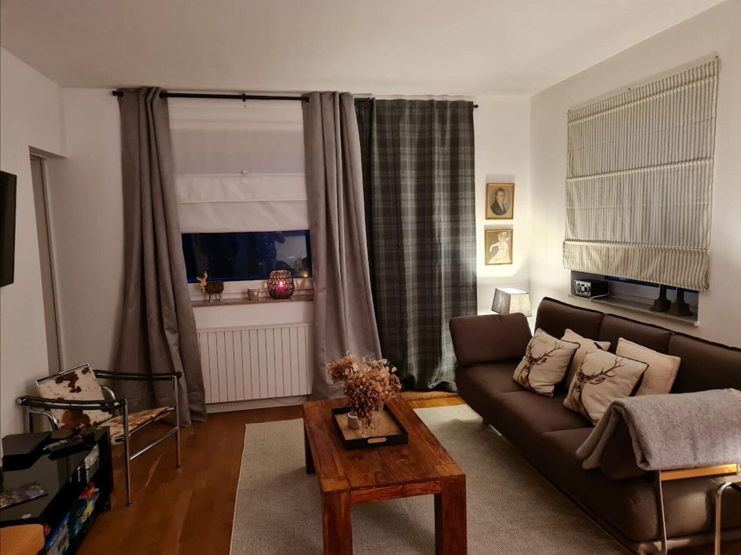 A living room with a sofa, a coffee table, a TV, and a window with curtains.