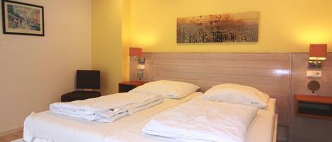 A hotel room with two beds, a headboard, bedside tables, a painting, and a ceiling light.