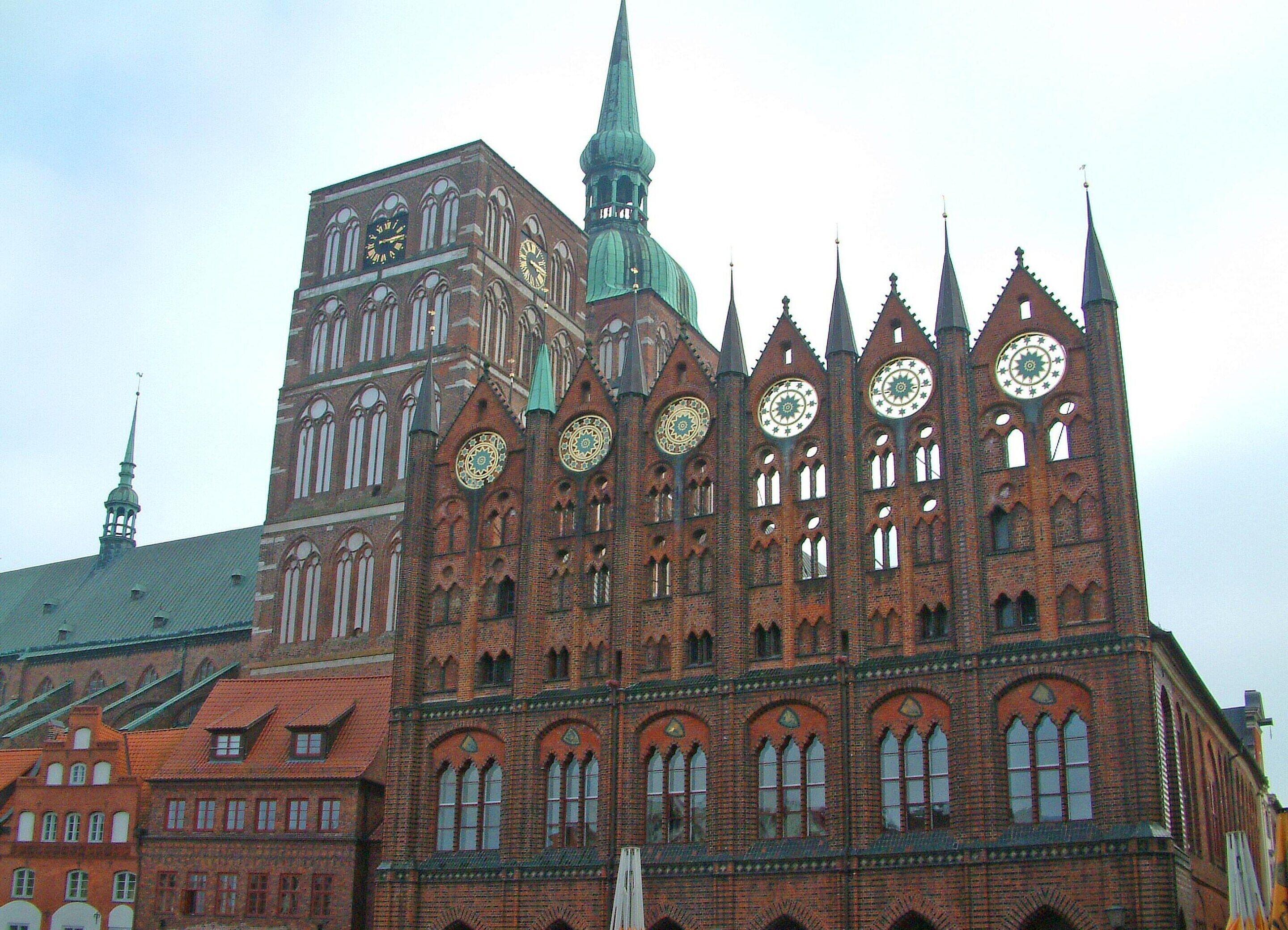 A historic building with multiple spires and large clocks, featuring Gothic architecture.