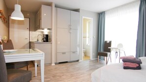 A modern hotel room with a bed, a desk with a chair, a kitchenette, and a bathroom. - Ferienwohnungen Grosser und Kleiner Seestern, Wiek (Wiek)