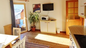 A cozy room with a wooden ceiling, a dining table with chairs, a potted plant, a microwave, a TV, and a wooden door. - Lovely Apartment in Tropolach With Sauna (Hermagor-Pressegger See)