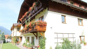 A multi-story building with wooden balconies, a covered porch, and a garden area with potted plants. - Lovely Apartment in Tropolach With Sauna (Hermagor-Pressegger See)