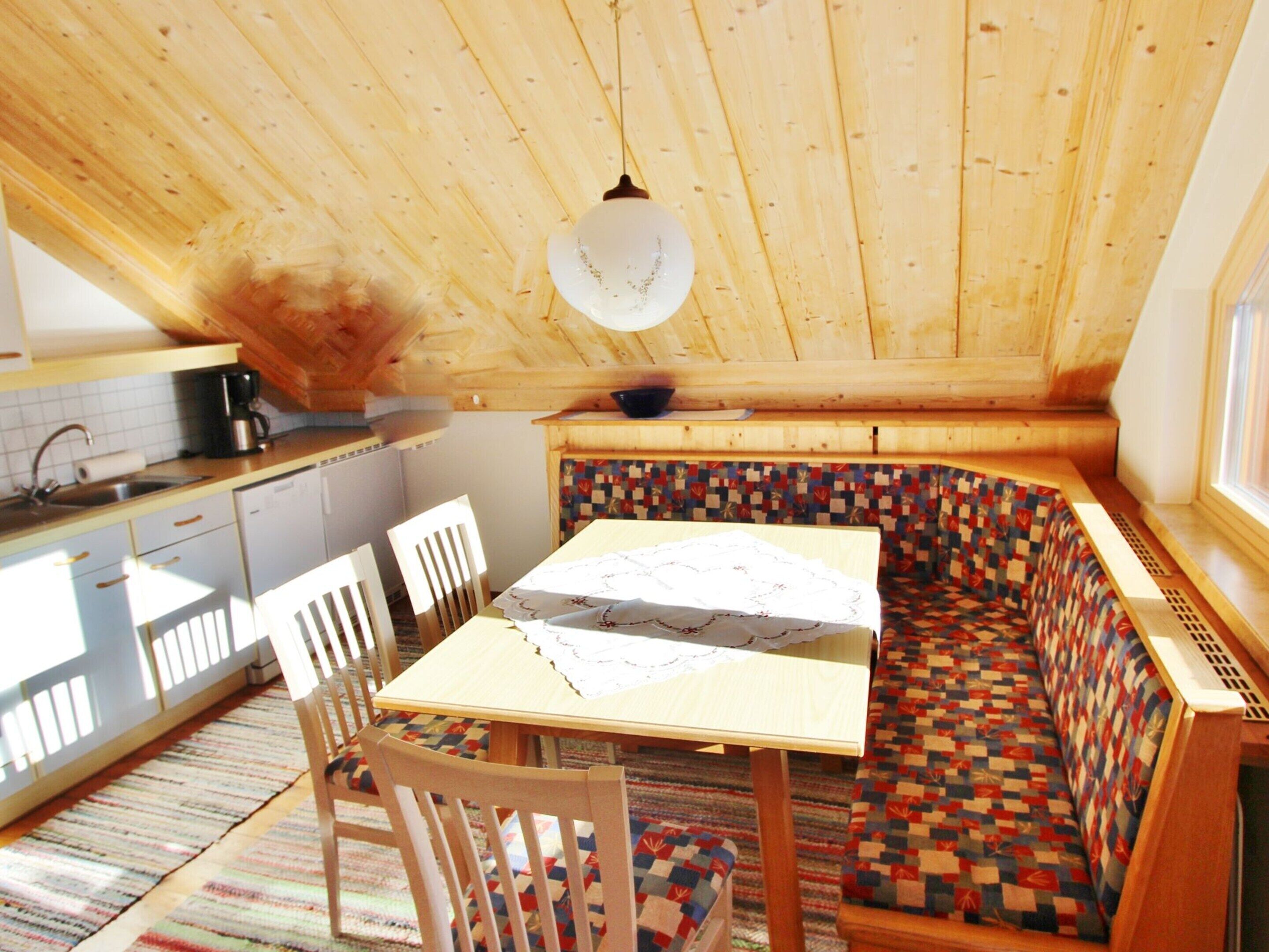 Una cocina acogedora con techo de madera, una mesa de comedor con sillas y un banco con un cojín acolchado y colorido.