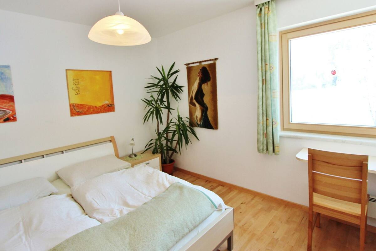 A bedroom with a bed, a desk, a chair, a hanging light, and artwork on the walls.