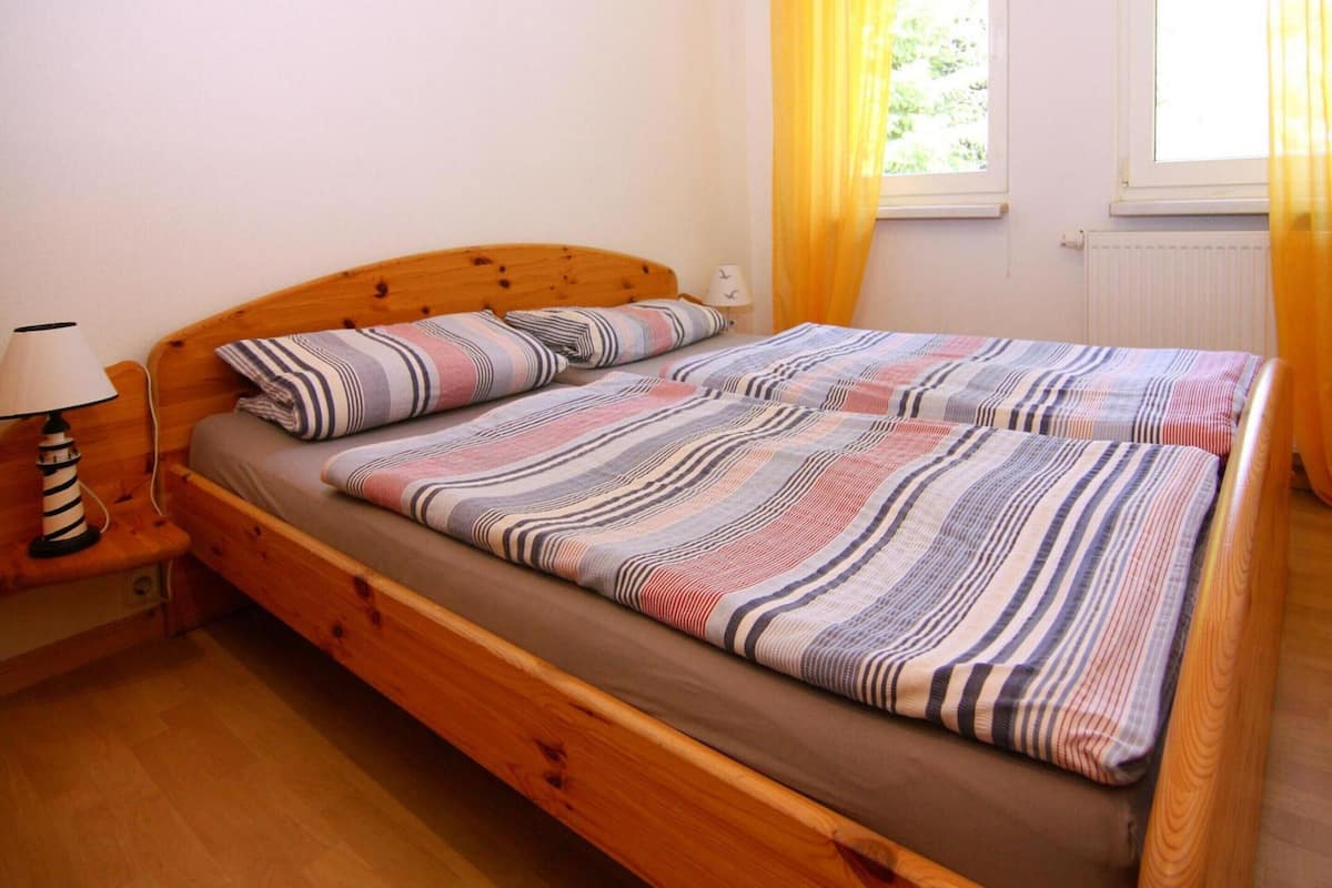 A single bed with a wooden frame, a bedside table with a lamp, and a window with yellow curtains.