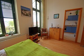 A room with a bed, a television, a chair, a small cabinet, and a view of a balcony.