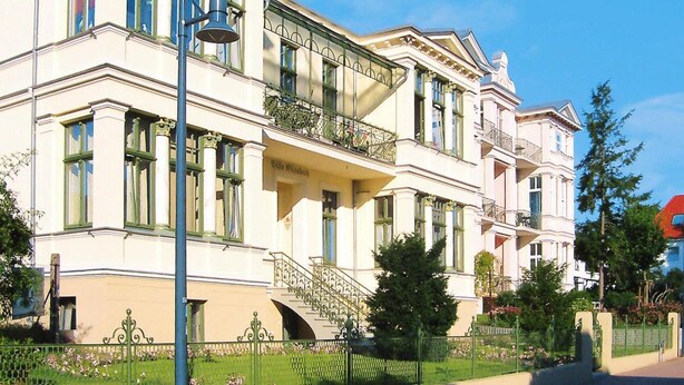 Um grande edifício de vários andares com arquitetura clássica, com varandas e uma escadaria central.
