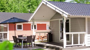 Un espacio de estar techado al aire libre con mesa, sillas, una parrilla y vistas a un edificio rojo.