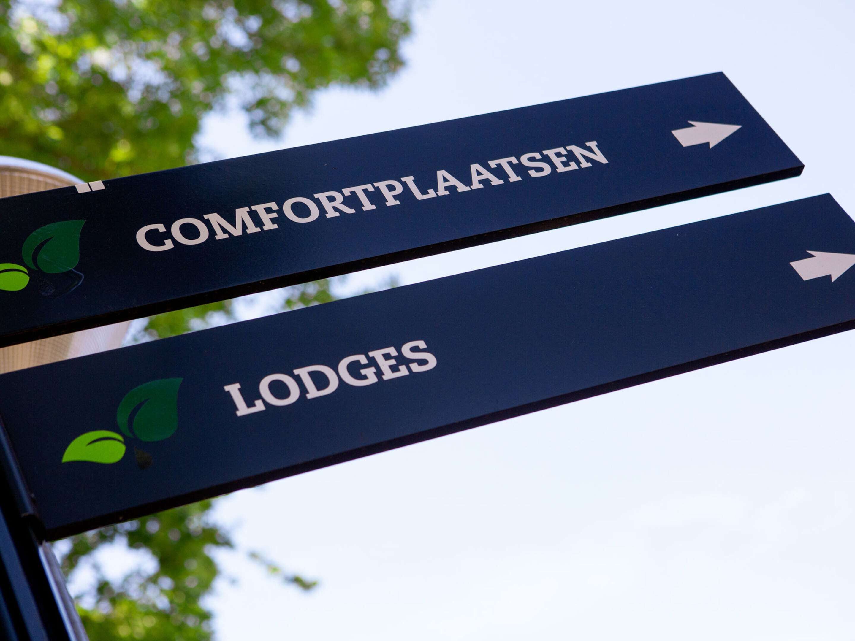 Directional signs for 'Comfortplaatsen' and 'Lodges' with arrows pointing to the right.