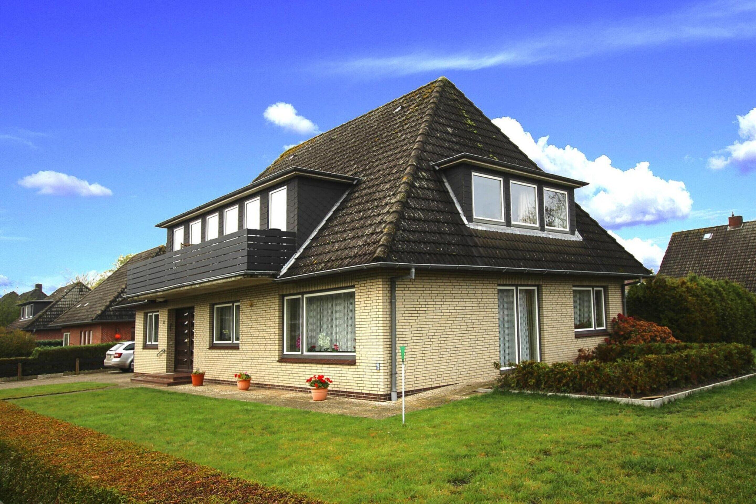 Ein zweistöckiges Haus mit geneigtem Dach, einer Veranda und einem kleinen Garten.