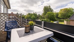 A balcony with a table, chairs, a potted plant, and a view of a garden and house. - Apartment, Tating (Tating)