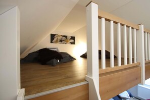 A bedroom with a sloped ceiling, wooden flooring, a white railing, and a painting of flowers on the wall. - Charmante Ferienwohnung mit Kamin in Zarchlin (Barkhagen)