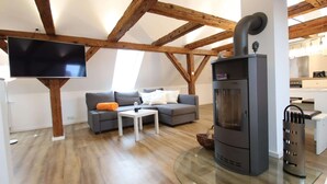 A modern living room with a flat-screen TV, a gray sofa, a white coffee table, and a wood-burning stove.