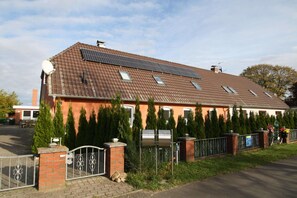 A residential building with a sloped roof, solar panels, a gated entrance, and a row of evergreen trees. - Charmante Ferienwohnung mit Kamin in Zarchlin (Barkhagen)
