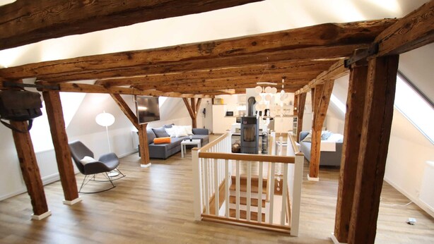 A loft-style living space with exposed wooden beams, a kitchen area, and a seating area with modern furniture.