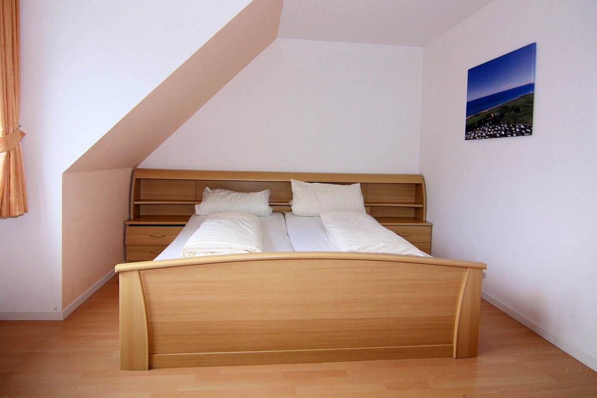 A bedroom with a wooden bed, white bedding, a wooden nightstand, and a painting on the wall.