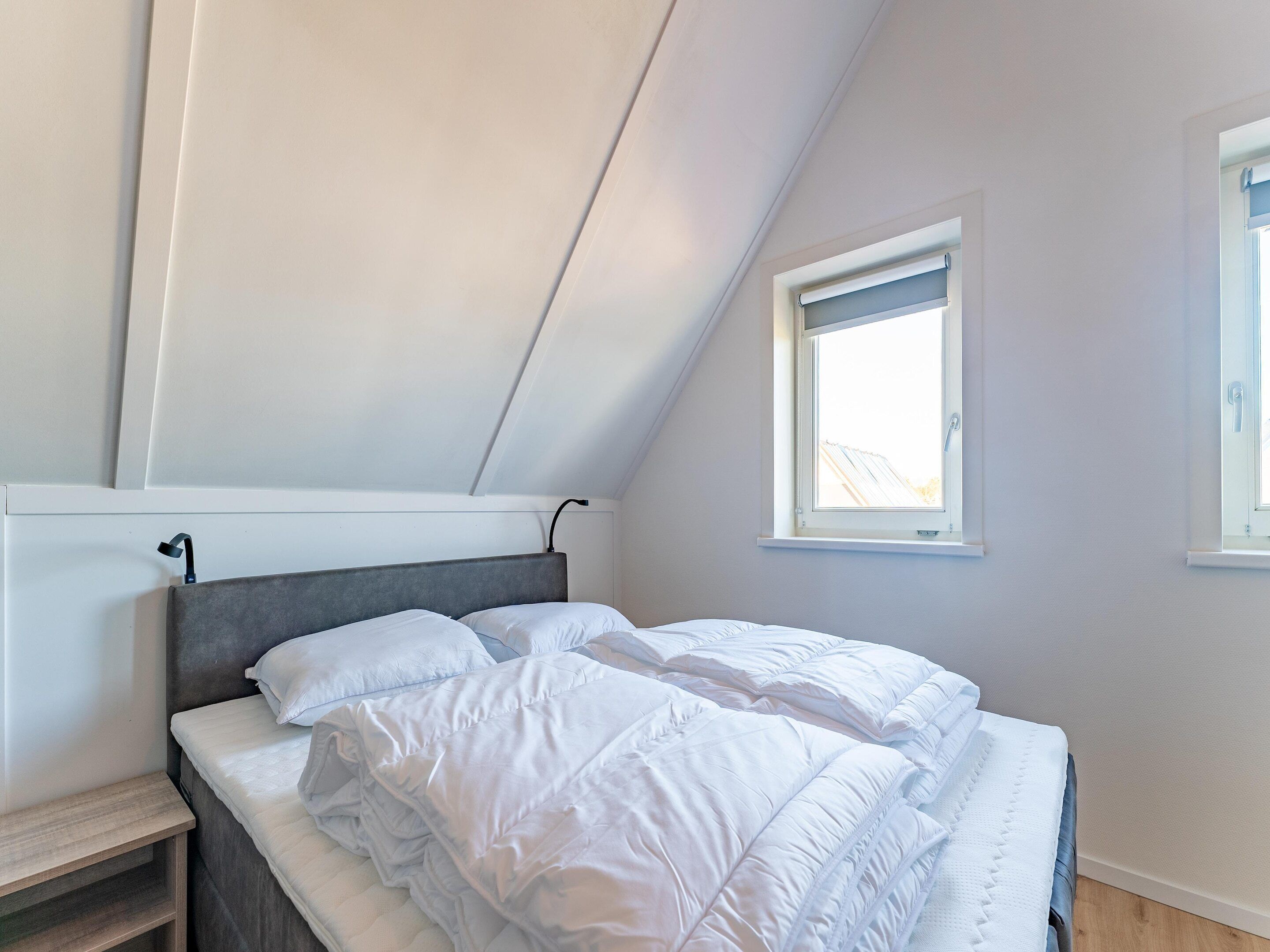 A bedroom with a sloped ceiling, a bed with white bedding, and a window providing natural light.