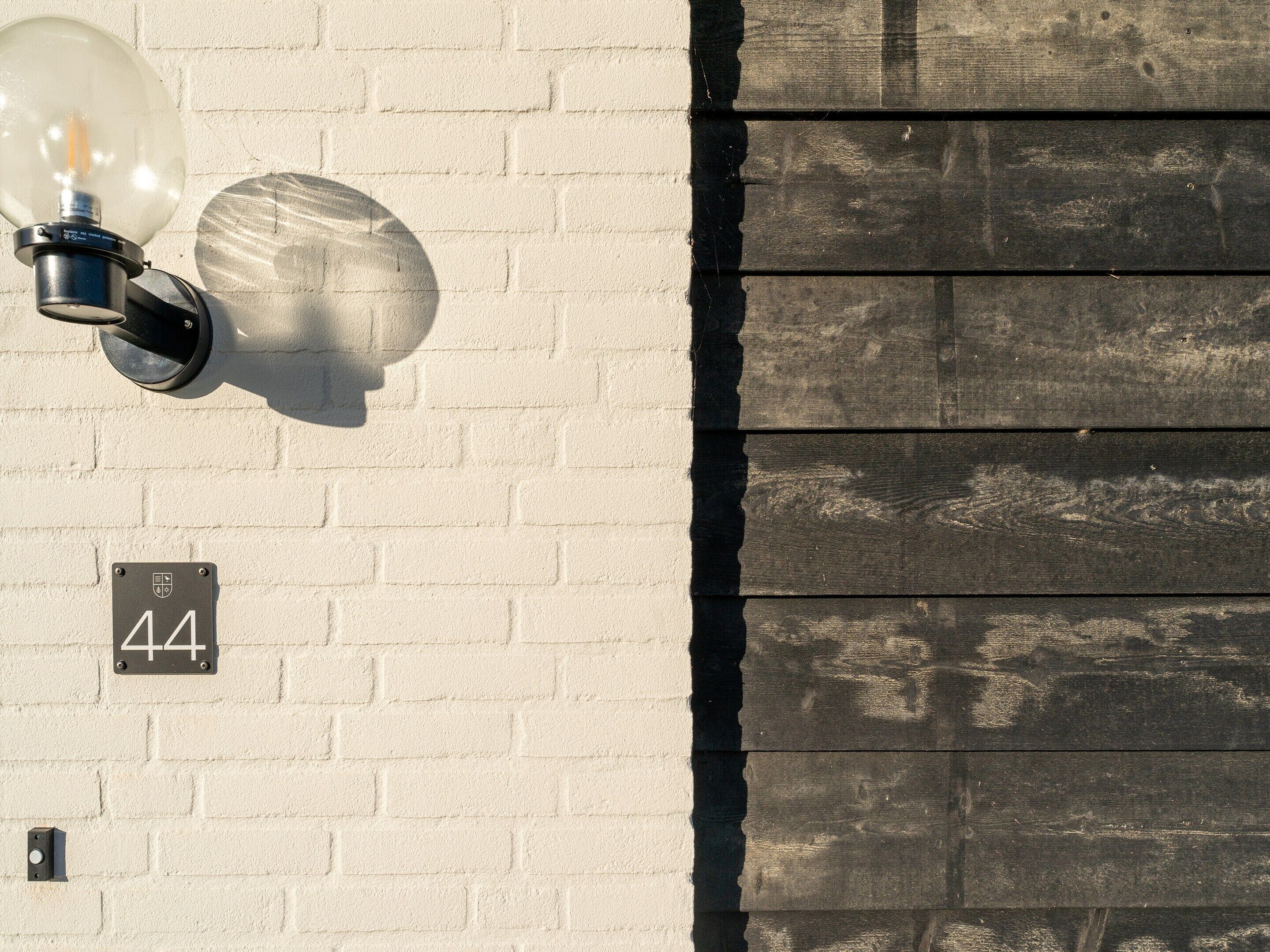 A wall-mounted light fixture and a house number sign on a brick wall.
