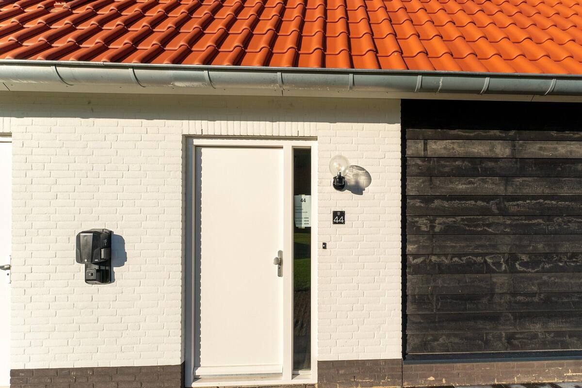 A building with a red-tiled roof, a white brick wall, a white door, and a black garage door.