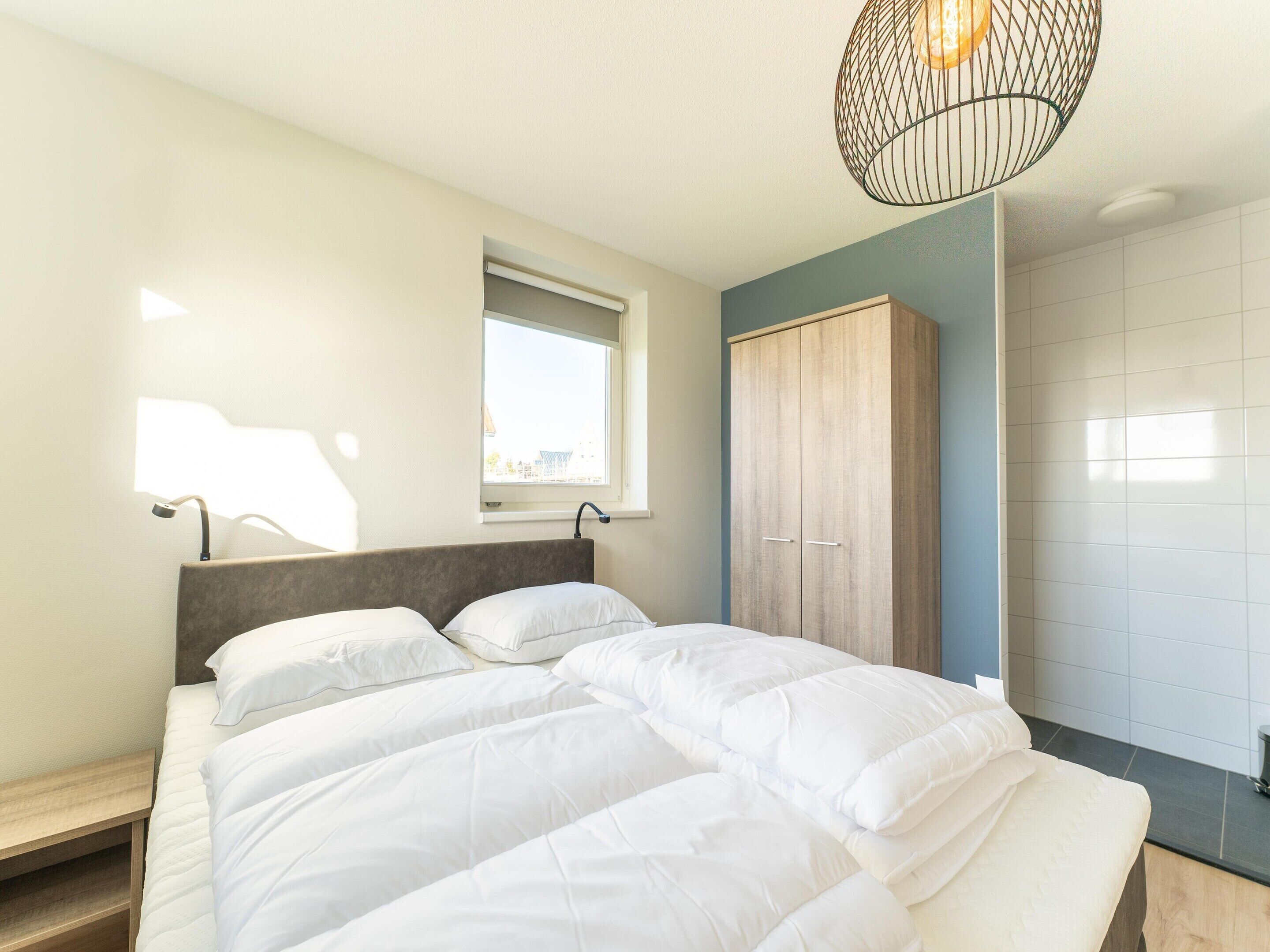 Une chambre à coucher avec un lit, une armoire, une fenêtre et un luminaire suspendu.