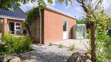 A brick house with a covered patio, a fenced garden, and a tree.