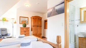 Ett hotellrum med en säng, en garderob i trä, en spegel, ett skrivbord och ett badrum med dusch.