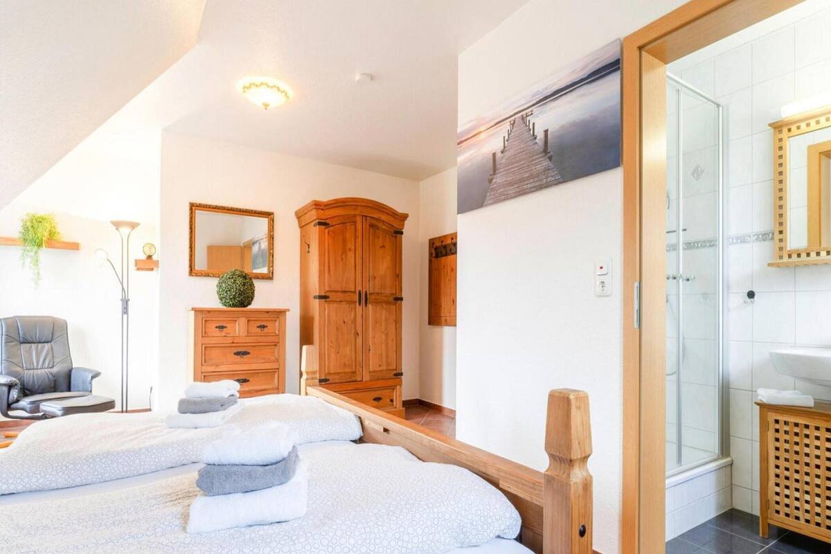 A hotel room with a bed, a wooden wardrobe, a mirror, a desk, and a bathroom with a shower.
