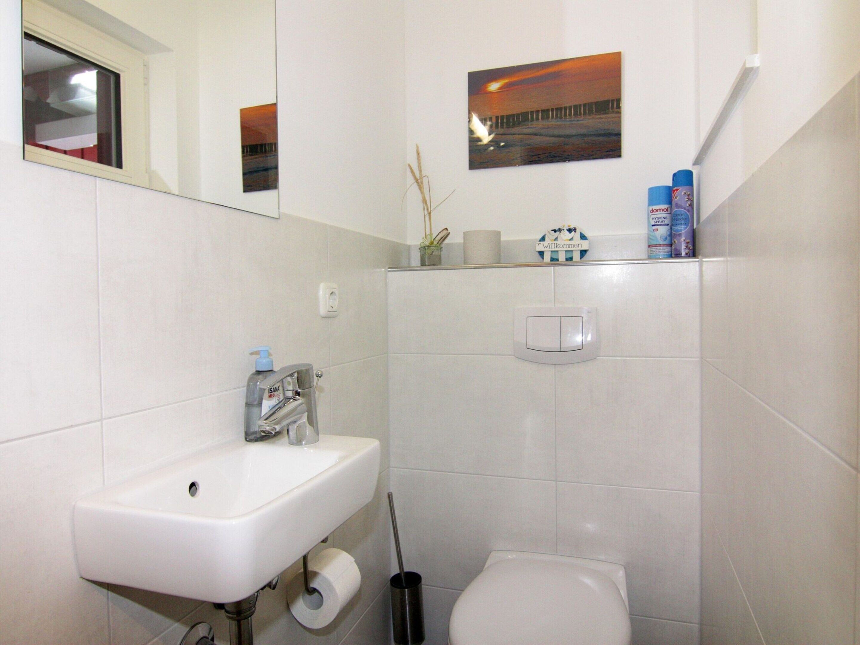 Ein Badezimmer mit Waschbecken, Toilette und Spiegel. An der Wand befinden sich Pflegeprodukte und ein Bild über dem Spiegel.
