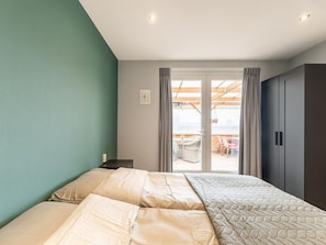 A bedroom with a bed, a nightstand, a wardrobe, and a sliding glass door leading to an outdoor area with a table and chairs.
