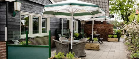 Un espace patio aménagé avec des meubles en osier, une table et un parasol vert et blanc.