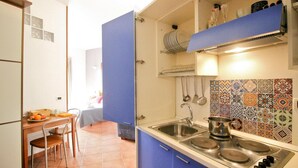 A compact kitchen with blue cabinets, a sink, and a stove. There is a dining table with chairs and a basket of fruit. - Holiday Flat in Central Location in Rome (Rome)